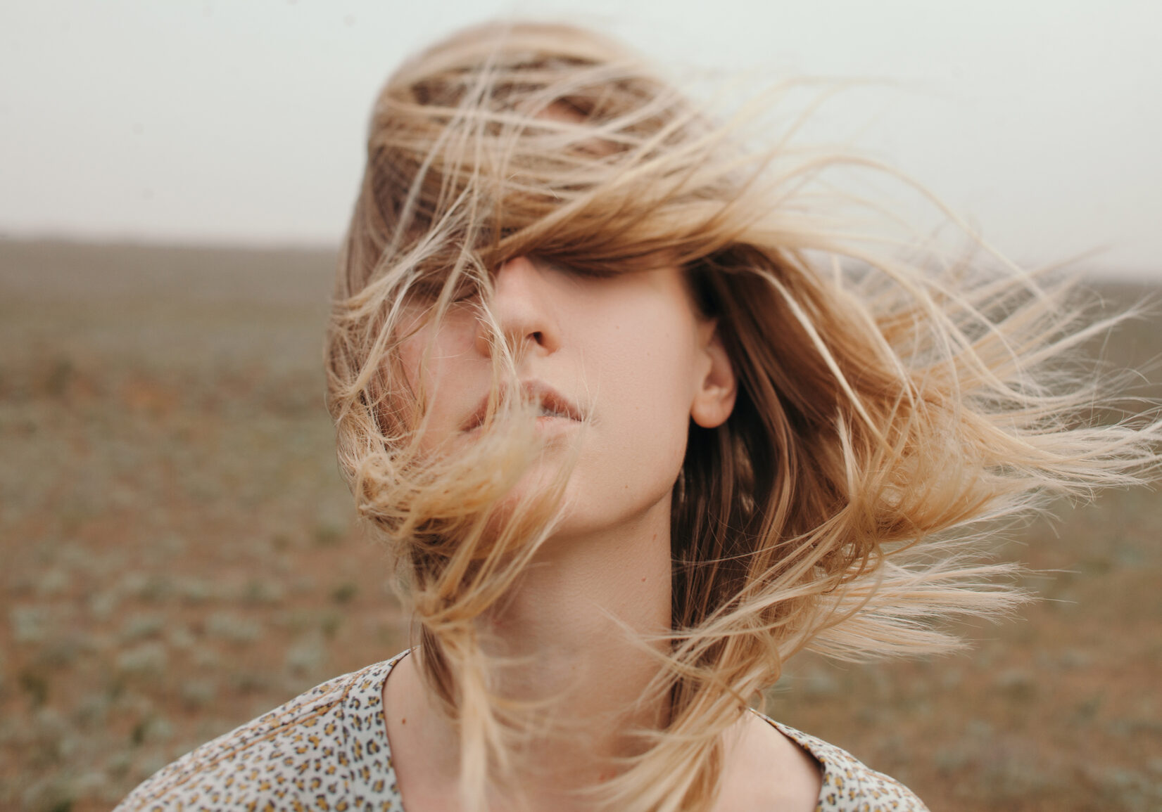 Portrait of blonde female wearing with her hair fluttering on wind and covering her face